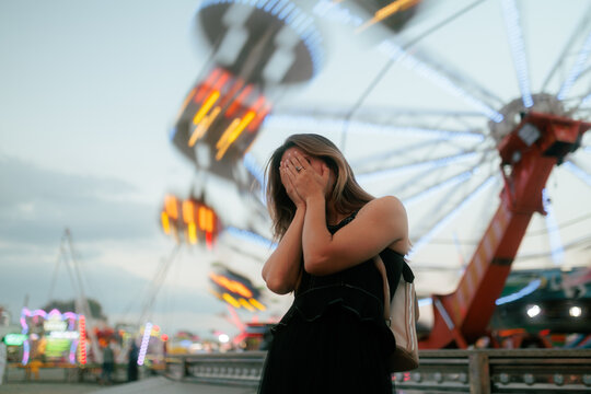  Woman Looking At Spinning Carousel In Amusement Park. Back view of a girl watching illuminated moving fairground rides during evening