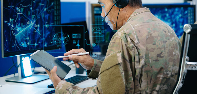 Senior military officer in camouflage using a tablet to analyze tactical radar data alongside his team in a modern cybersecurity command center.