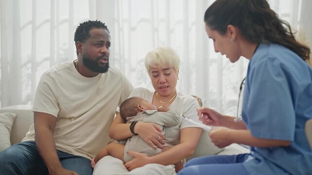 Nurse in blue scrubs leans in to check a newborn baby's heartbeat with a stethoscope while the mother cradles the infant and the father looks on with quiet concern.