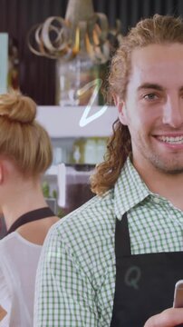 Animation of letters moving over caucasian man using cellphone and woman making coffee in cafe