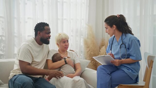 Nurse sat in a chair, writing patient notes on a clipboard, while a cross-cultural couple held their sleeping baby on a sofa.