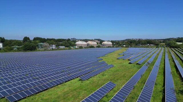 Plymouth, Devon, England: The drone flies high over the top of a solar panel farm and onwards towards a sewage farm and industrial estate in the background. Plymouth is a busy UK port.