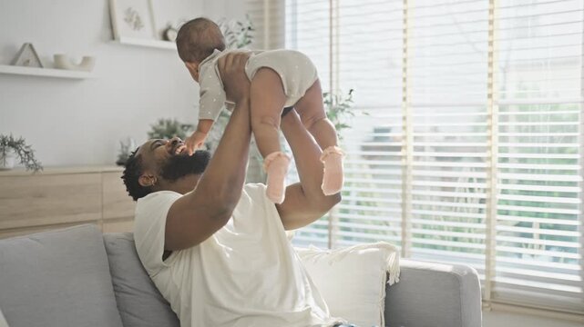 Father sits on the sofa cradling his newborn baby against his chest, sharing a quiet bonding moment together in a bright modern family living room at home.