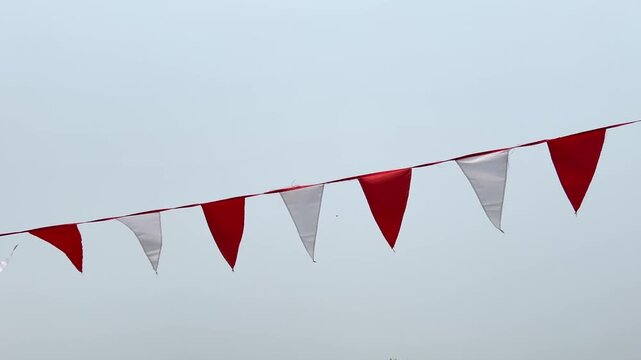 Red and white flags fluttering in the wind against a clear blue sky on a bright sunny day.
