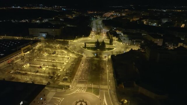 Aerial view of a busy roundabout at night with city lights and traffic motion.