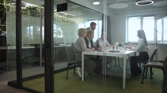 A view through a glass partition shows a modern, busy office interior. Job interview process is in office. Human resources, meeting and group of hiring candidates for vacancy
