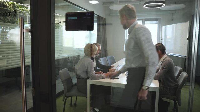 A view through a glass partition shows a modern, busy office interior. Job interview process is in office. Human resources, meeting and group of hiring candidates for vacancy