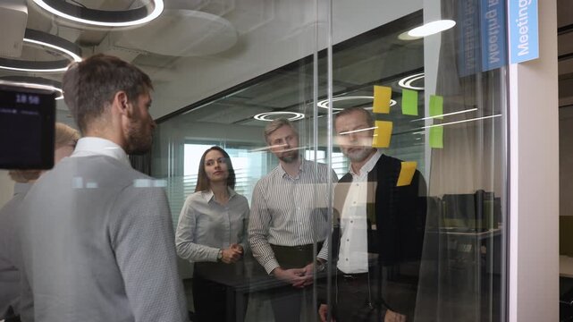 Businesspeople talking in their diverse team during a brainstorming session with sticky notes on glass wall in a modern office
