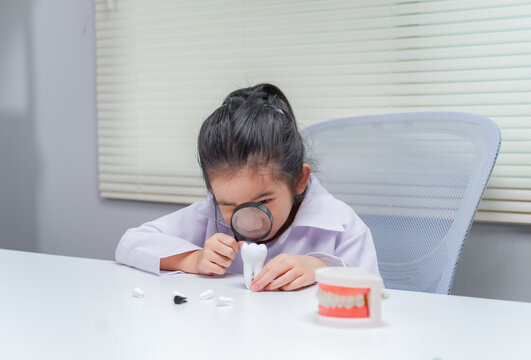 Little girl using magnifying glass inspecting toy teeth for dental health checkup in educational healthcare setting	