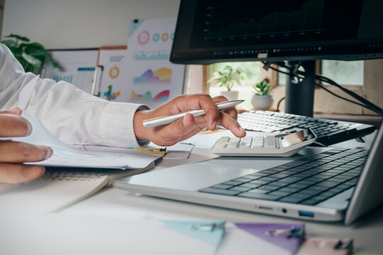 Business professional using a calculator while reviewing financial documents beside a laptop, representing accounting, budgeting, financial analysis, business planning, and numerical decision making