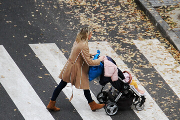 Madre con carro de bebé cruzando paso de peatones y hojas de otoño mamá peatón cruzar paso de cebra y maternidad © Diego