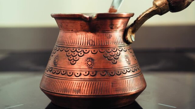 Traditional copper cezve with ornate engraved patterns brewing Turkish coffee that froths and overflows at the top. High quality 4k footage