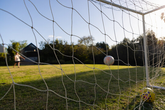 soccer net view of teenage boy striking soccer ball into net at sunset