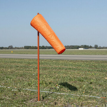 Orange windsock on a mast beside an empty grass runway