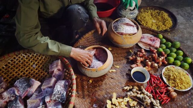 Traditional Vietnamese braised fish preparation in Vu Dai village, Ninh Binh, with fresh fish, galangal, ginger, chilies, limes, and spices arranged on a woven mat.