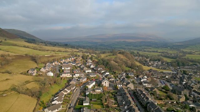Aerial drone footage of picturesque welsh village nestled within green rolling hills of brecon beacons national park landscape.