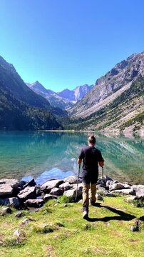 Hiker walking towards mountain lake with scenic reflections and peaks- Lake Gaube- vertical video