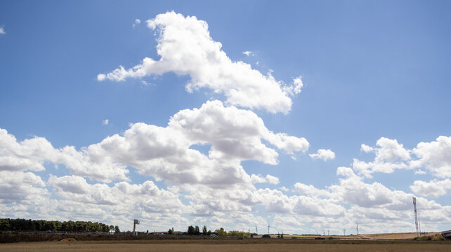 Amplio cielo azul con nubes blancas sobre un campo y &aacute;rboles en el horizonte