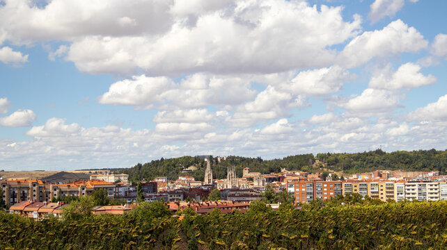 Vista de una ciudad con edificios y catedral bajo un cielo azul con nubes y campo verde en Burgos, Espa&ntilde;a