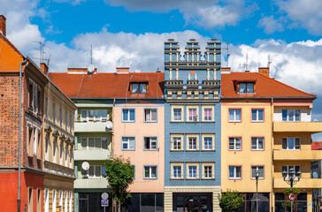 Obraz premium Row of colorful city tenements in Brzeg featuring decorative blue facade with renaissance attic wall, red tile roofs, blue sky with white clouds background in bright sunlight.