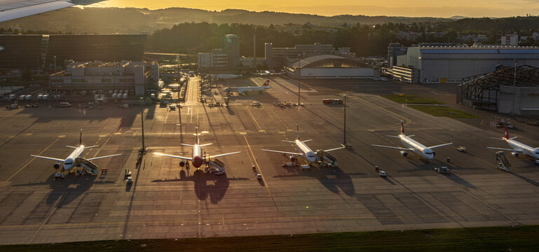 Zurich, Switzerland - 13 June 2026: Aerial view of Zurich Airport with multiple commercial airplanes parked on the tarmac during golden hour, featuring hangars and service vehicles.
