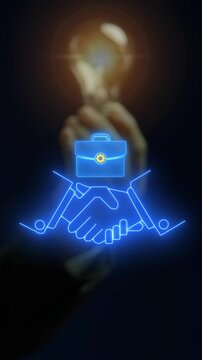 Businessman hand holding glowing lightbulb vertical shot above handshake partnership and briefcase. Creative business deal, innovative corporate agreement, and joint venture inspiration concept.