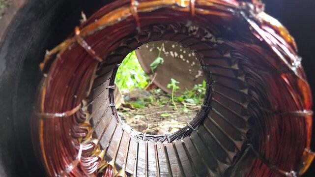 Tunnel View Through Copper Winding Stator Core of an Electric Motor Stator Housing Lying Outdoors on Dirt Ground, Highlighting Industrial Scrap, E-Waste Recycling, & Discarded Power Machinery Hardware
