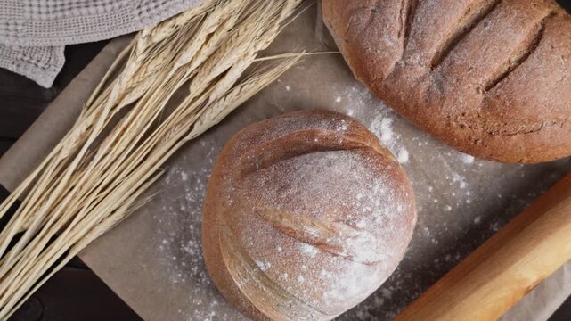 Slow camera movement reveals fresh artisan bread, wheat stalks, flour, a wooden rolling pin and knife arranged on a rustic table, creating a traditional homemade baking scene