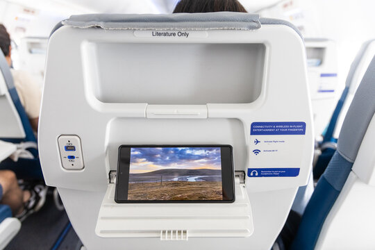 Perspective view of passenger watching movie on smart phone placed on back of front seat during long haul flight