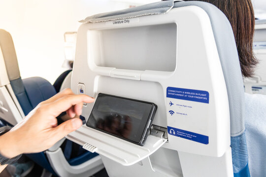 Passenger finger operating smart phone placed on back seat during flight long haul flight.