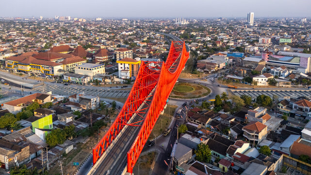 Banjarsari, Indonesia - 13 August 2026: Aerial view of the prominent red steel bridge structure spanning over the urban landscape with surrounding roads, buildings, and residential areas.
