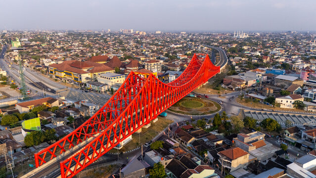 Banjarsari, Central Java, Indonesia - 13 August 2026: Aerial view of the bright red Flyover Manahan truss bridge spanning over the urban landscape with surrounding buildings and roads.