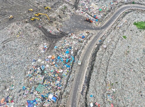 Dhaka, Bangladesh - 27 August 2026: Aerial view of Aminbazar Landfill with heavy machinery and excavators operating among large piles of waste near a winding road.
