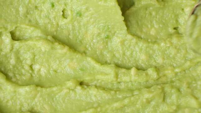 Top view of a spoon gliding through fresh green guacamole to show its texture.