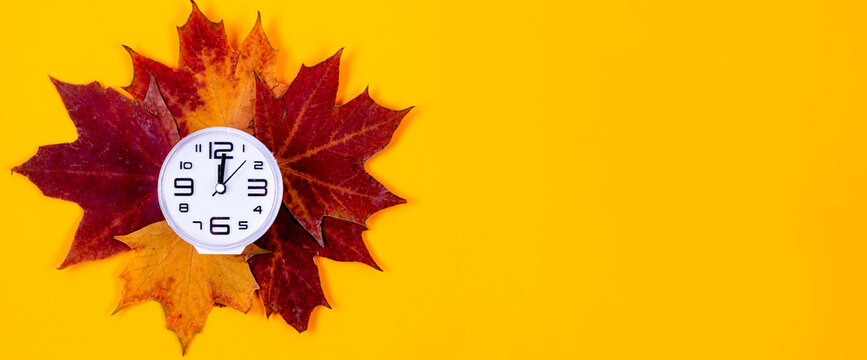 Clock and autumn leaves on yellow background, saving winter time concept