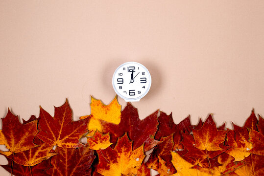 Clock and autumn leaves on beige background, saving winter time concept