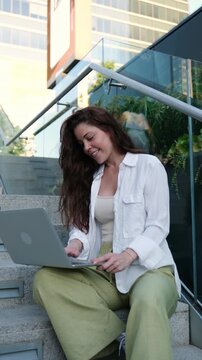 Young businesswoman typing on her laptop while sitting on the stairs in a modern urban environment