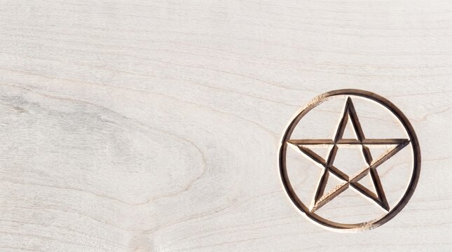 Carved five pointed star pentagram symbol on light wooden surface represents spiritual protection.