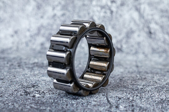 Industrial cylindrical roller bearing standing upright on rough textured concrete surface.
