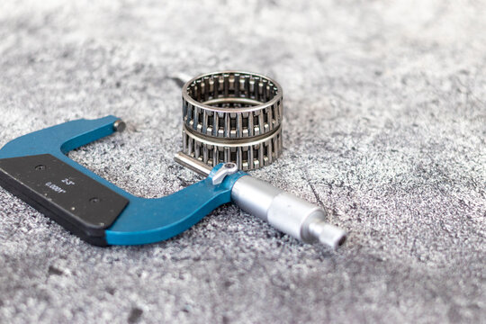 Precision outside micrometer caliper lying near stacked needle roller bearings on workshop workbench.