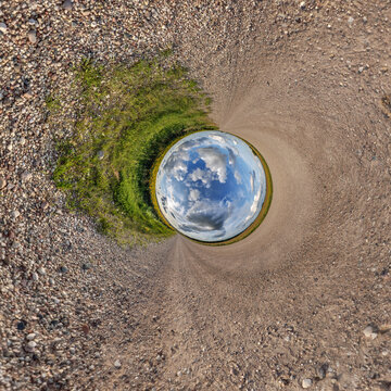creative tiny planet photo of a rural landscape with dirt road, green fields, and cloudy sky forming a circular world.