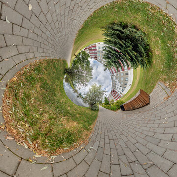 creative tiny planet photo of a rural landscape with dirt road, green fields, and cloudy sky forming a circular world.