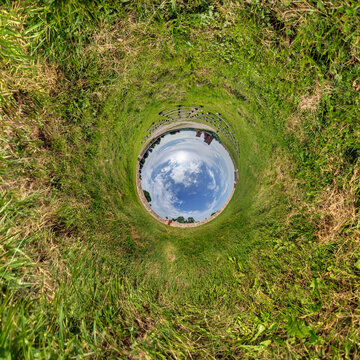 creative tiny planet photo of a rural landscape with dirt road, green fields, and cloudy sky forming a circular world.