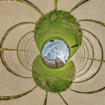 creative tiny planet photo of a rural landscape with dirt road, green fields, and cloudy sky forming a circular world.