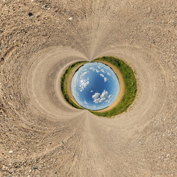creative tiny planet photo of a rural landscape with dirt road, green fields, and cloudy sky forming a circular world.
