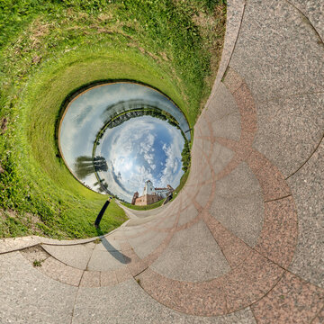 creative tiny planet photo of a rural landscape with dirt road, green fields, and cloudy sky forming a circular world.
