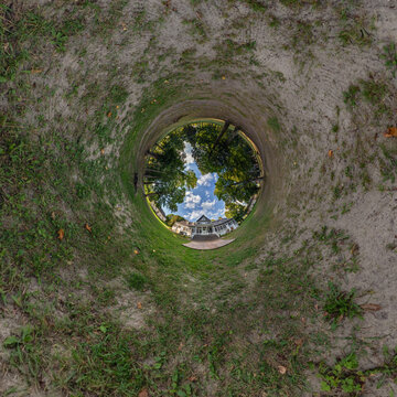 creative tiny planet photo of a rural landscape with dirt road, green fields, and cloudy sky forming a circular world.