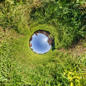 creative tiny planet photo of a rural landscape with dirt road, green fields, and cloudy sky forming a circular world.