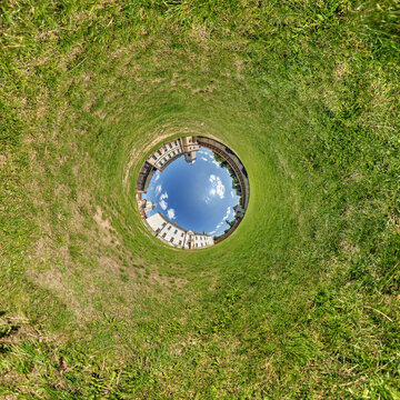 creative tiny planet photo of a rural landscape with dirt road, green fields, and cloudy sky forming a circular world.