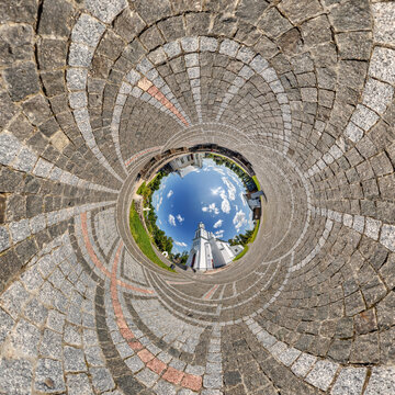 creative tiny planet photo of a rural landscape with dirt road, green fields, and cloudy sky forming a circular world.
